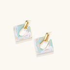 Geometric square enamel earrings with marbled turquoise and lavender pattern, gold U-shaped connector on cream background.